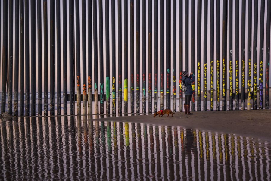 A Woman walking  her dog takes a Photograpoh of the border fence that seperates  San Diego, CA and Tijuana, Mexico 