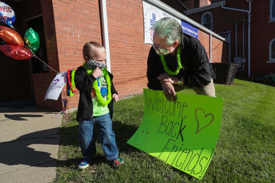 Clark Harrison, chairman, holds a welcome sign and greets Weston Bourne upon arrival at The Village Early Childhood Education Center, Liberty Street, California, Pa., on June 1, 2020.  Prior to opening day, children were invited to select and vote on hair colors for the staff and administration.  They selected the color green for Harrison.