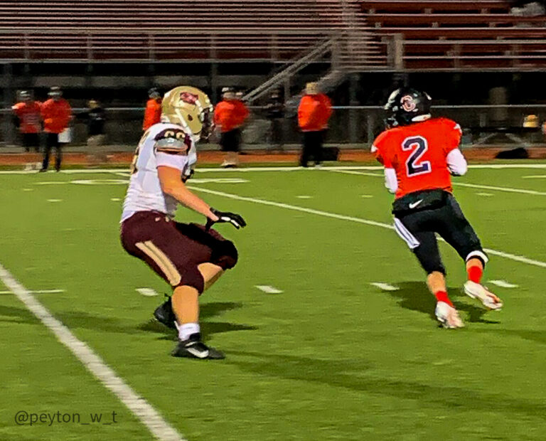 Junior quarterback Brendan Harps (#2, red), scrambles away from the pressure applied by senior linemen Zach David (#66, white) to look for an open receiver down the field.