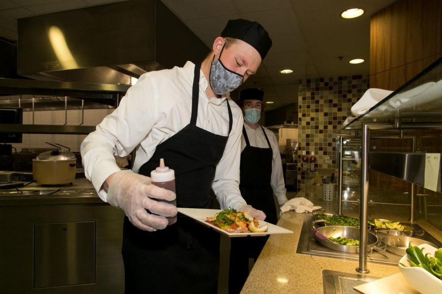 Cal U Professional Golf Management (PGM) students Nolan Bistline (on left) and Brendan Halpin prepare to serve a plate of orange chicken stir fry in the Gold Rush dining hall, Natali Student Center, April 21. 2021.