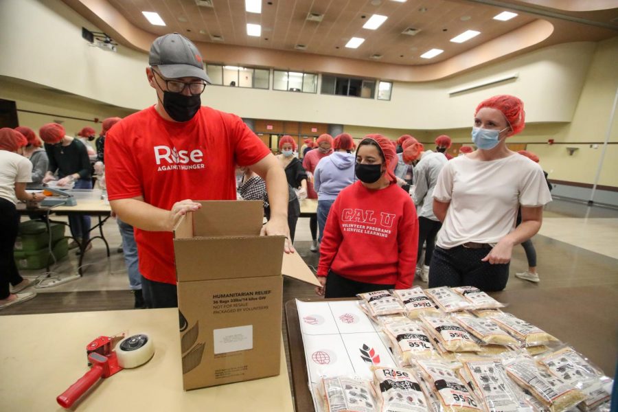 Joey Kelly, community engagement manager, Rise Against Hunger, Pittsburgh, with Cal U students Maria Dovshek and Bailey Westfall, preparing a box for meal packages that will be sent to international locations.  Cal U volunteers aimed to create 10, 000 packages at the event in the Natali Student Center, Nov. 17, 2021