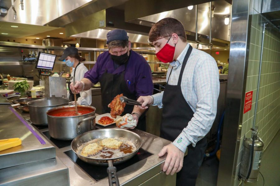 (From left) Nicholle Schuerman, sophomore, Dave Herforth, AVI Chef, and Cale Kauffman, sophomore, in the kitchen preparing chicken parmesan and fettucini with marinara sauce for the Professional Golf Management Dinner in the Gold Rush dining hall of the Natali Student Center, March 1, 2022.