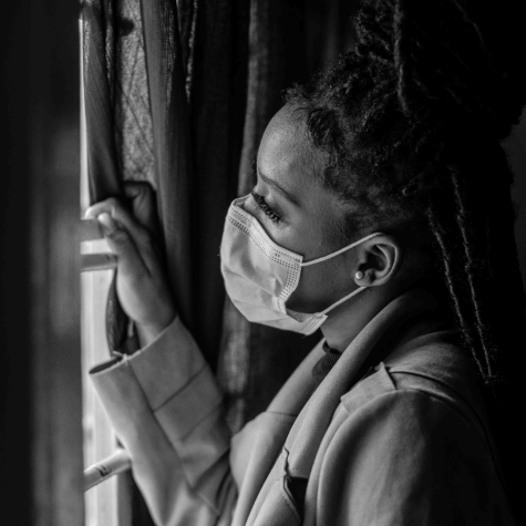 A woman wearing a mask staring out the window.