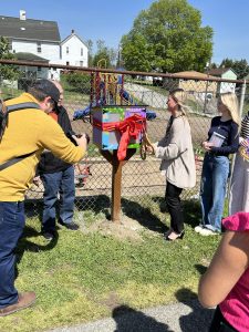 Izabella DeGlopper, President of NSSLHA, with a pair of scissors cutting the ribbon to commence the opening of the Little Library. 