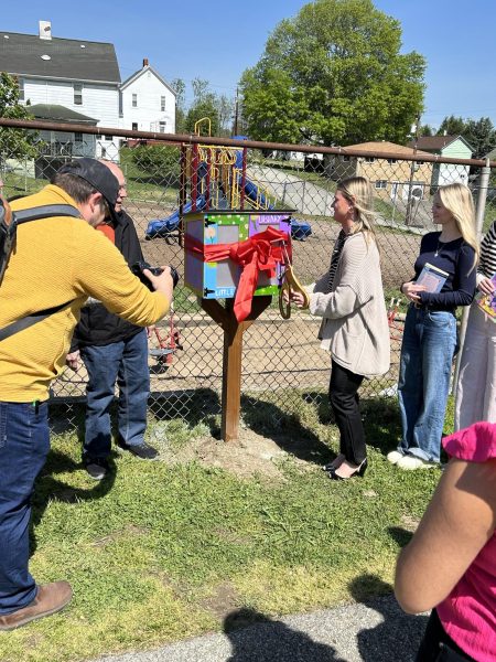 Izabella DeGlopper, President of NSSLHA, with a pair of scissors cutting the ribbon to commence the opening of the Little Library. 